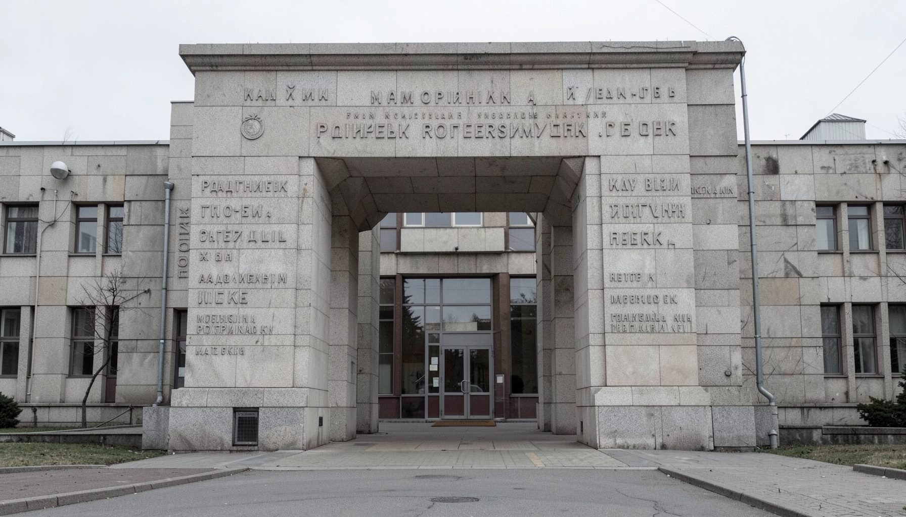 Входная группа мемориального комплекса с каменной аркой и высеченными именами защитников, строгие линии, приглушённые серые и бежевые тона