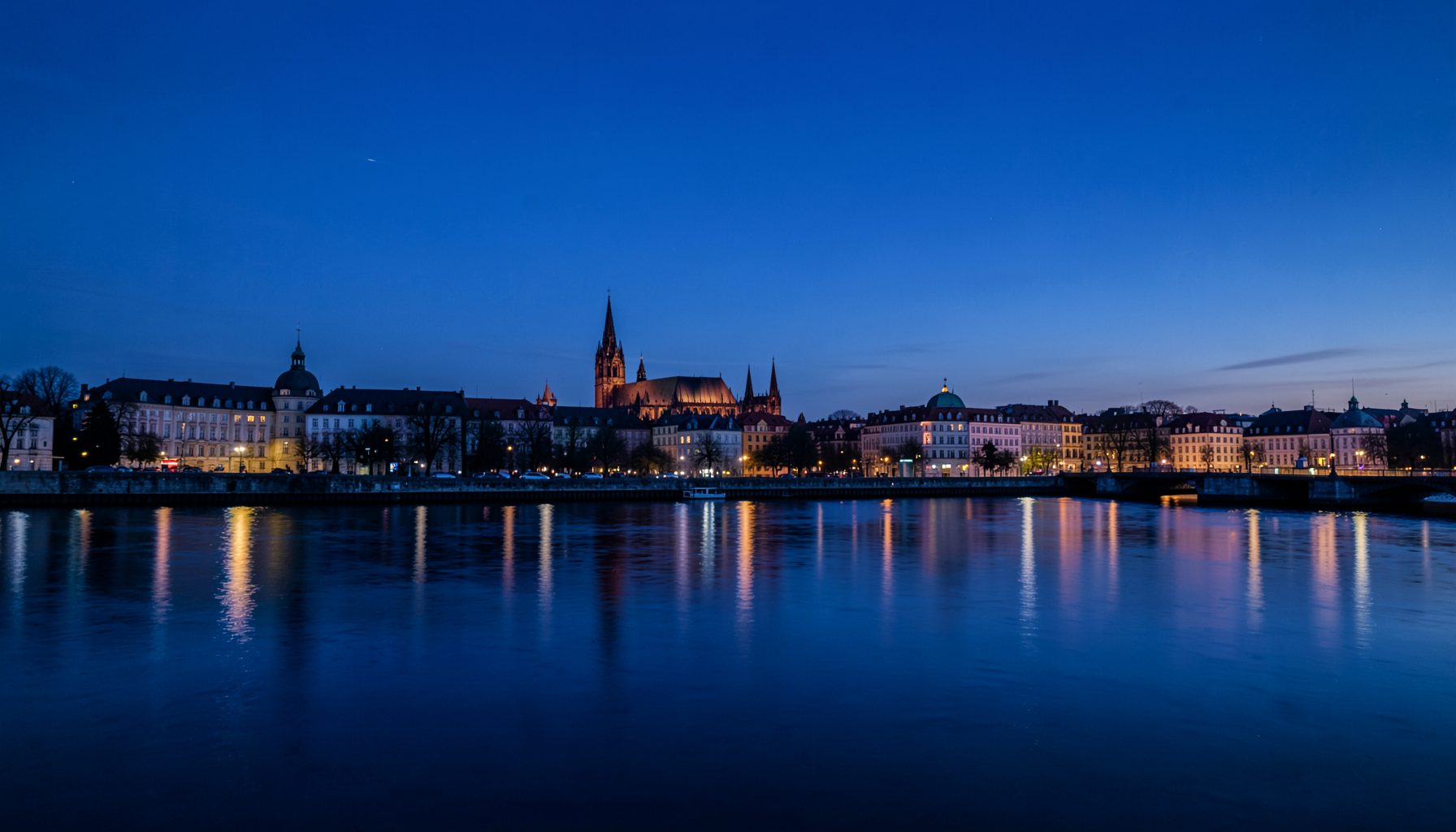 Панорама Кёльна с силуэтом знаменитого готического собора на фоне вечернего неба глубокого синего цвета, отражающегося в спокойных водах Рейна